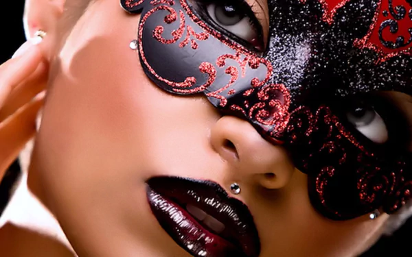 A close-up of a masked individual showcases deep red lips adorned with glossy lipstick and piercings, set against a dramatic dark background, creating an intriguing visual impact.