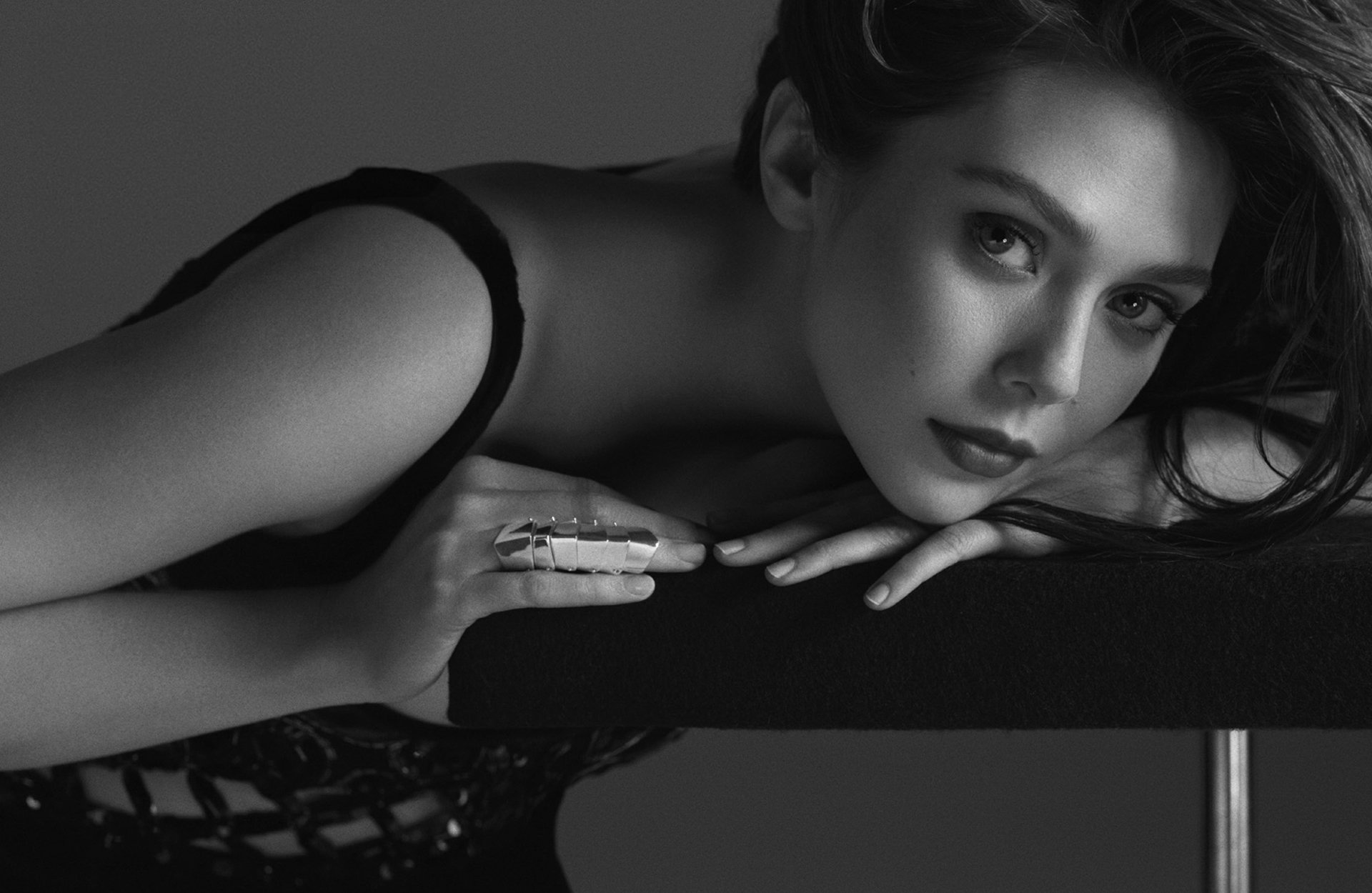 A striking black and white HD wallpaper featuring Elizabeth Olsen, posed elegantly with one hand resting on a surface, showcasing her captivating gaze and refined style.