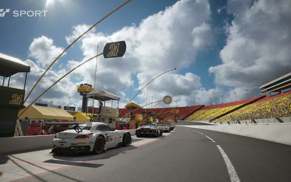 Gran Turismo Sport HD PC desktop wallpaper: GT race cars lined in the pit lane at a sunlit stadium circuit beneath dramatic clouds.