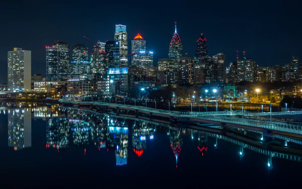 Nighttime view of Philadelphia’s illuminated skyscrapers reflecting in the water, captured in stunning 4K Ultra HD as a vibrant cityscape wallpaper.
