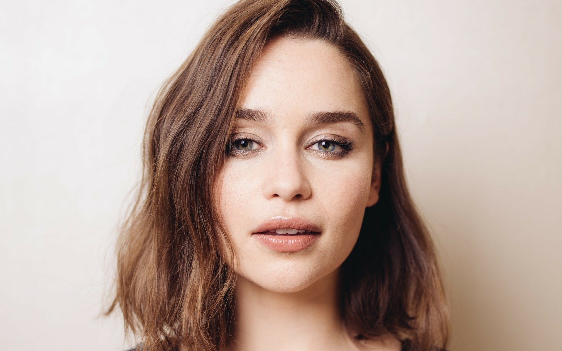 HD PC desktop wallpaper featuring a close-up portrait of celebrity Emilia Clarke with natural makeup and soft lighting against a neutral background.