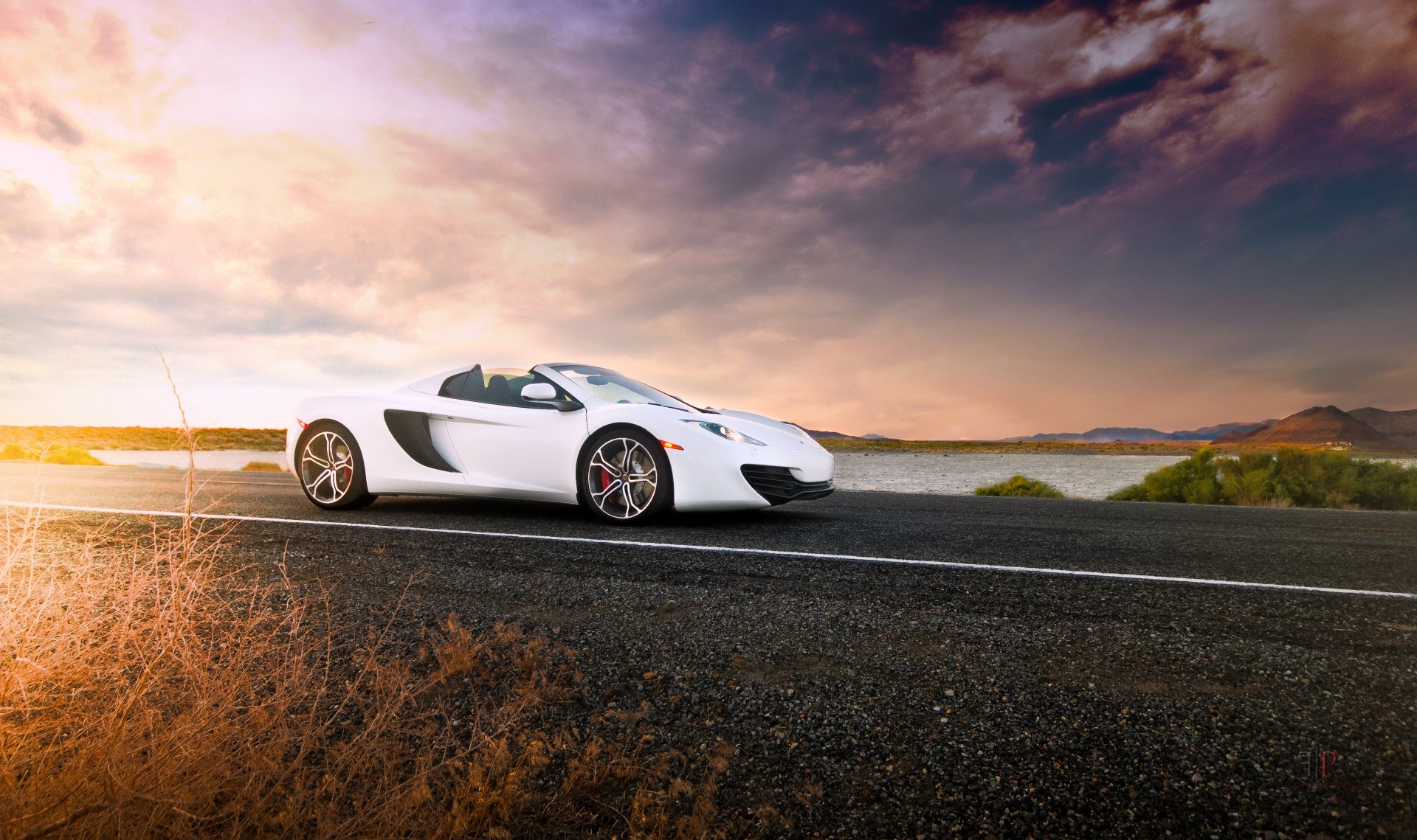 A white McLaren MP4-12C Spider supercar parked on a coastal road under a dramatic sky, captured in high-definition for a PC desktop wallpaper.