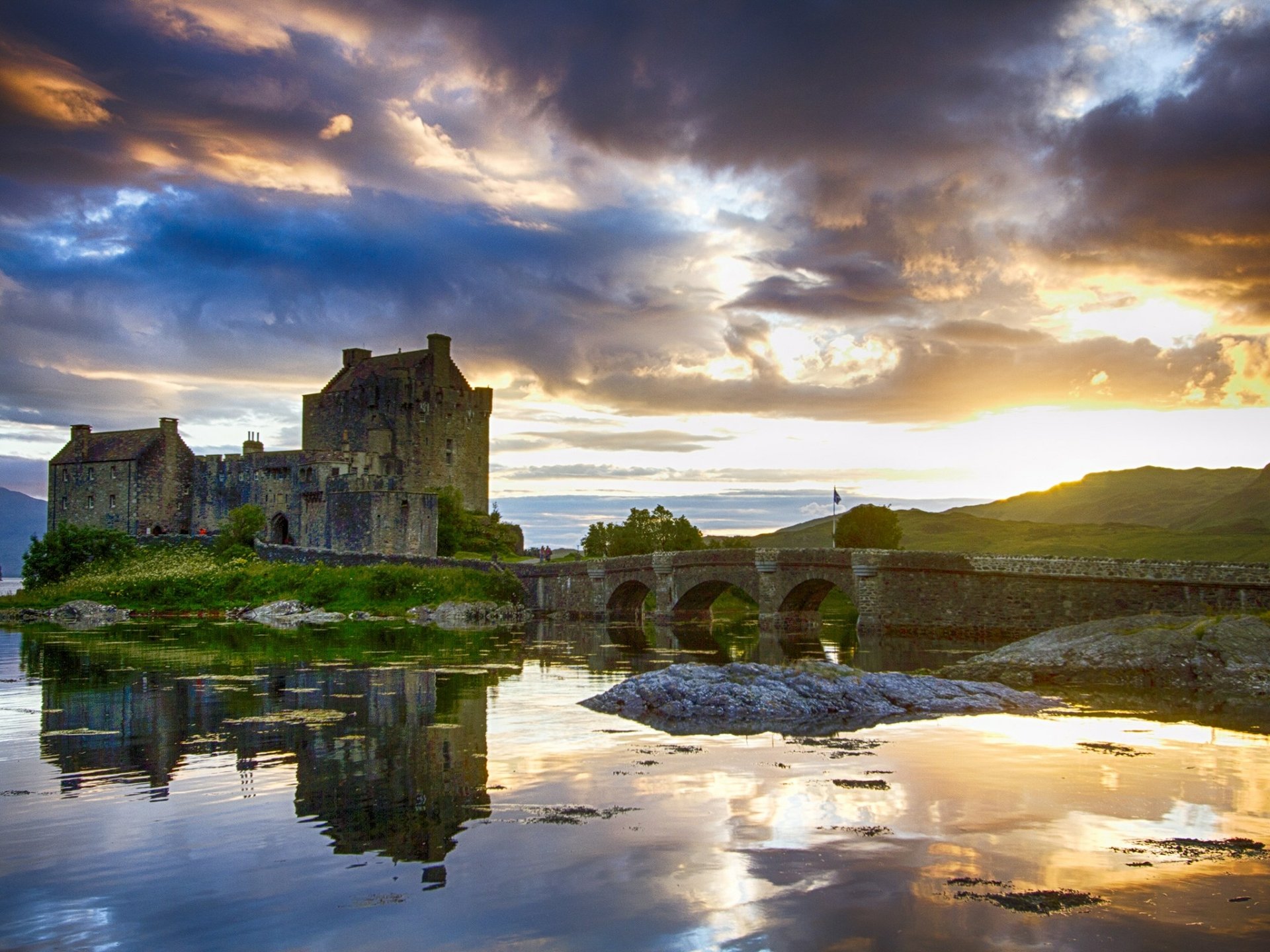 HD desktop wallpaper featuring the man-made Eilean Donan Castle at sunset, reflected in calm waters under a dramatic sky.