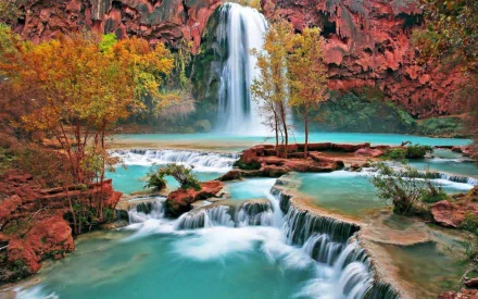 HD nature wallpaper featuring a serene waterfall cascading into turquoise pools surrounded by autumnal trees and rocky formations, designed as a desktop background.