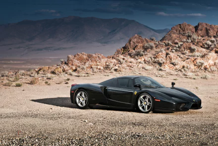 Black Ferrari Enzo supercar vehicle parked on a desert plain with rocky hills, 2K Quad HD PC desktop wallpaper background.
