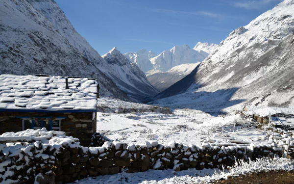 Snow-covered hut and stone wall in a winter landscape of snowy mountains in Nepal under a clear blue sky, captured in HD mountain photography.
