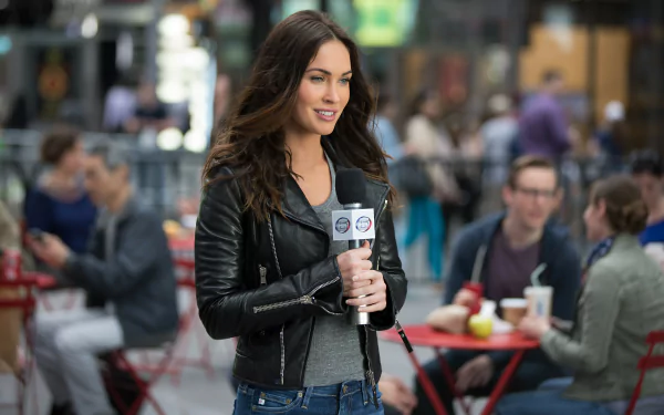 Megan Fox portrays April O’Neil in *Teenage Mutant Ninja Turtles: Out of the Shadows*, reporting on the streets, set against a vibrant urban background.