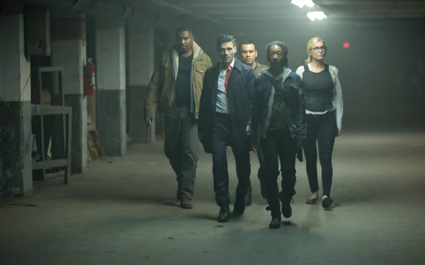 Five determined figures walk through a dim concrete parking garage in a scene from the movie The Purge: Election Year — 5K Ultra HD PC desktop wallpaper/background.