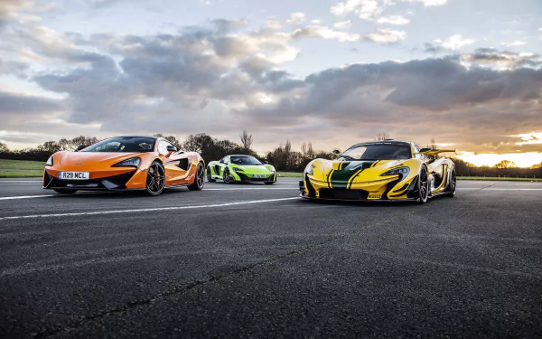 Three McLaren supercars—an orange 570S, a green variant, and a striking yellow and black model—parked on a racetrack against a dramatic sunset backdrop. 4K Ultra HD quality.