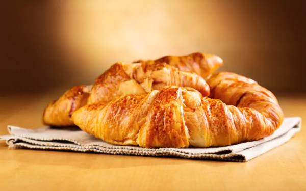 Close-up of golden croissants on a napkin, breakfast food; 4K Ultra HD PC desktop wallpaper and background.