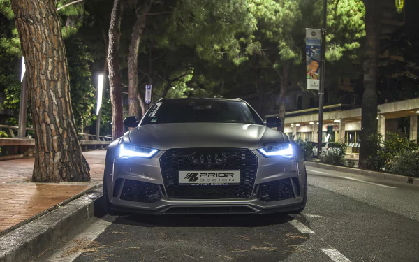 Front view of a silver Audi RS6 parked on a tree-lined street at night, showcasing its sleek design and illuminated headlights as an HD PC desktop wallpaper.