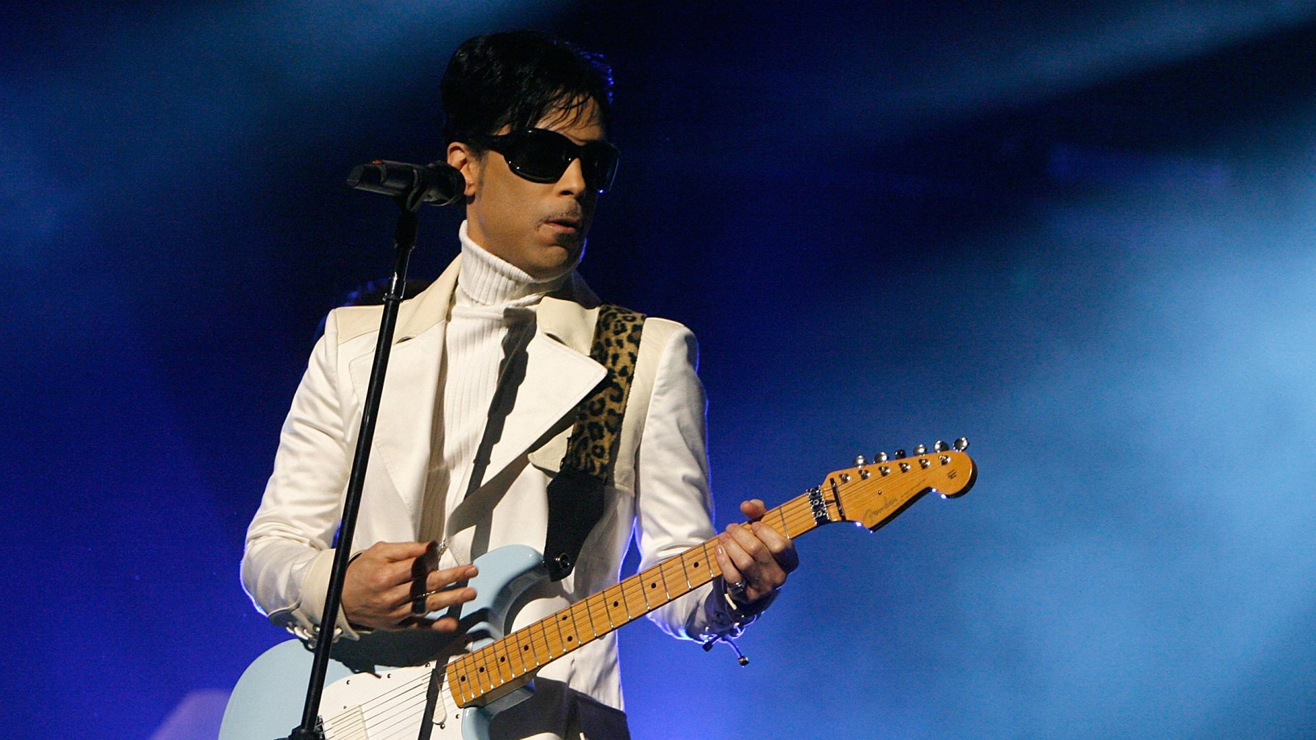 HD desktop wallpaper of musician and singer Prince performing on stage with electric guitar, captured in vibrant blue lighting.