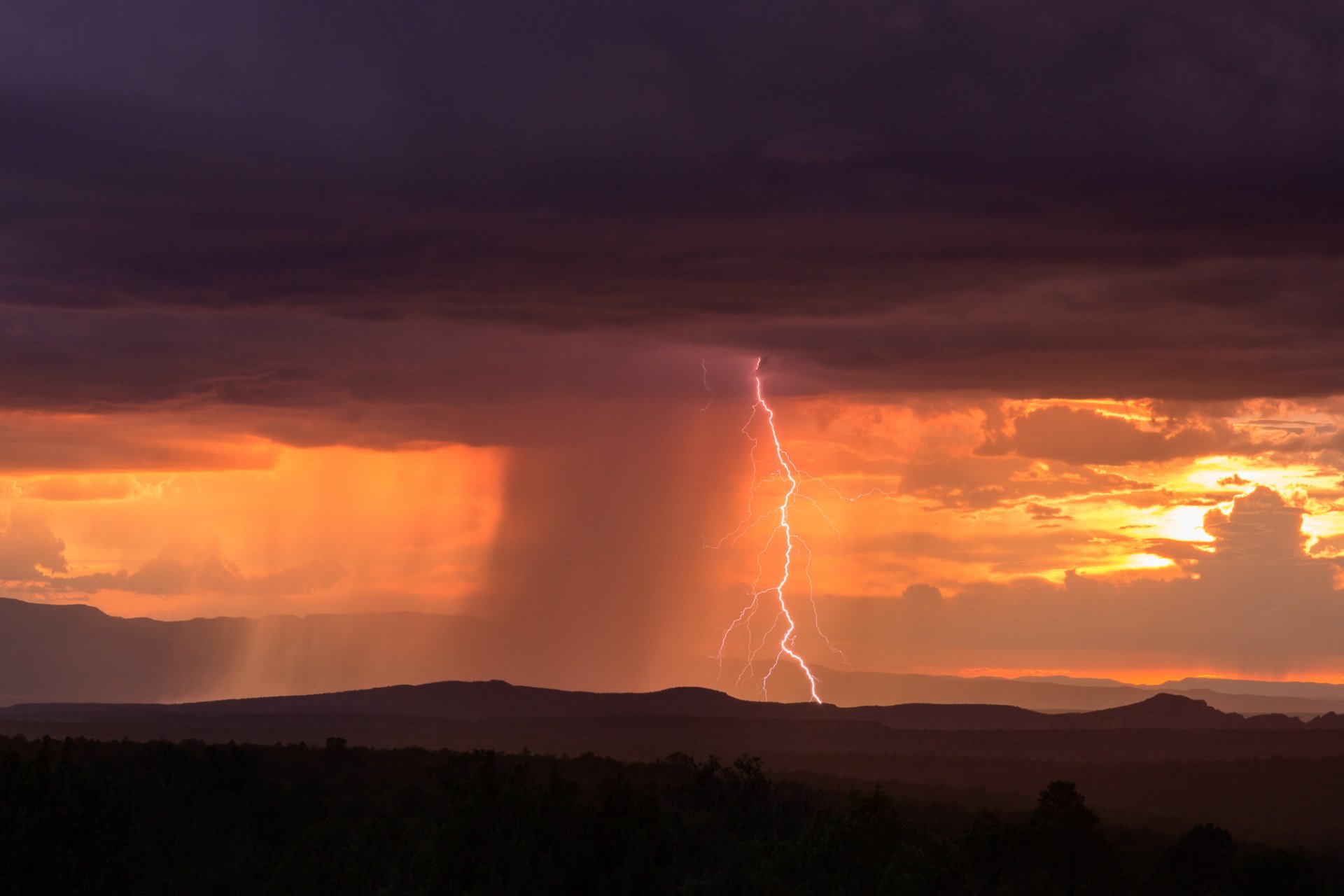 HD desktop wallpaper: dramatic landscape photography of storm clouds and a lightning bolt over silhouetted hills at sunset.