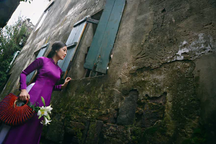 Vietnamese model in a vibrant purple Ao Dai holding lilies, standing against a weathered wall, captured in 4K Ultra HD for a PC desktop wallpaper.
