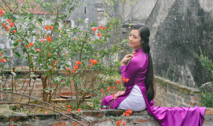 A Vietnamese woman in a vibrant purple Ao Dai sits beside blooming spring flowers, captured in sharp 4K Ultra HD for a stunning desktop wallpaper.