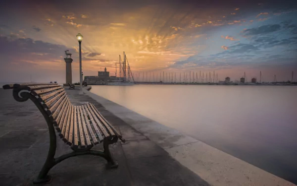 4K Ultra HD desktop wallpaper showing a man-made waterfront with a bench, lighthouse, and boats under a colorful sunset sky.