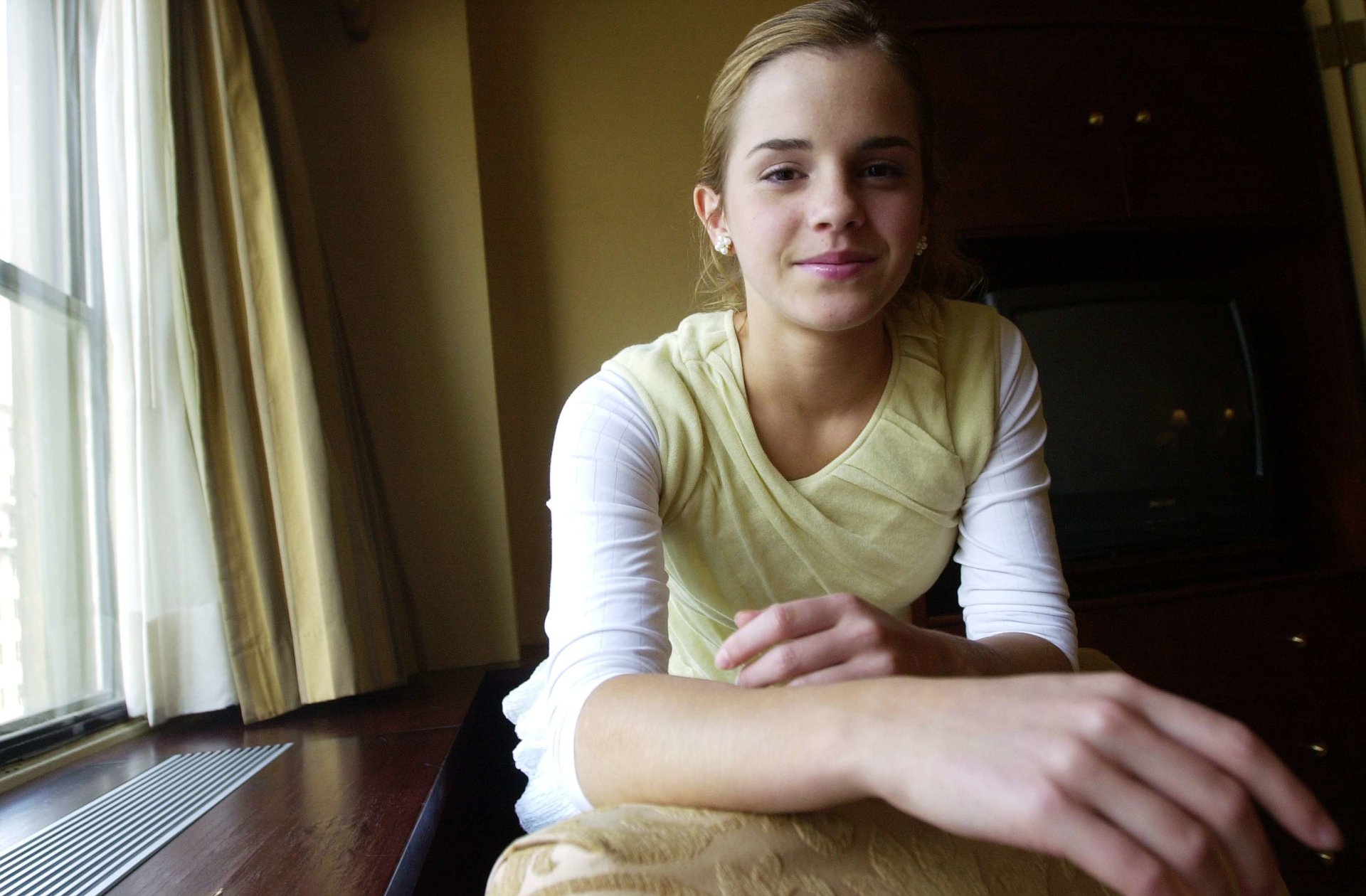 High-definition desktop wallpaper featuring Emma Watson, smiling and relaxed, seated near a window with curtains drawn.