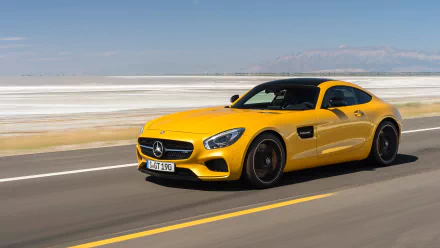 Yellow Mercedes-AMG GT grand tourer driving on a road with a scenic, expansive landscape in the background, captured in high-definition quality.