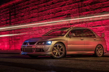 A Mitsubishi Lancer Evolution is showcased in a striking HD desktop wallpaper, illuminated by vibrant red lighting against a textured wall, highlighting its sleek design and sporty features.
