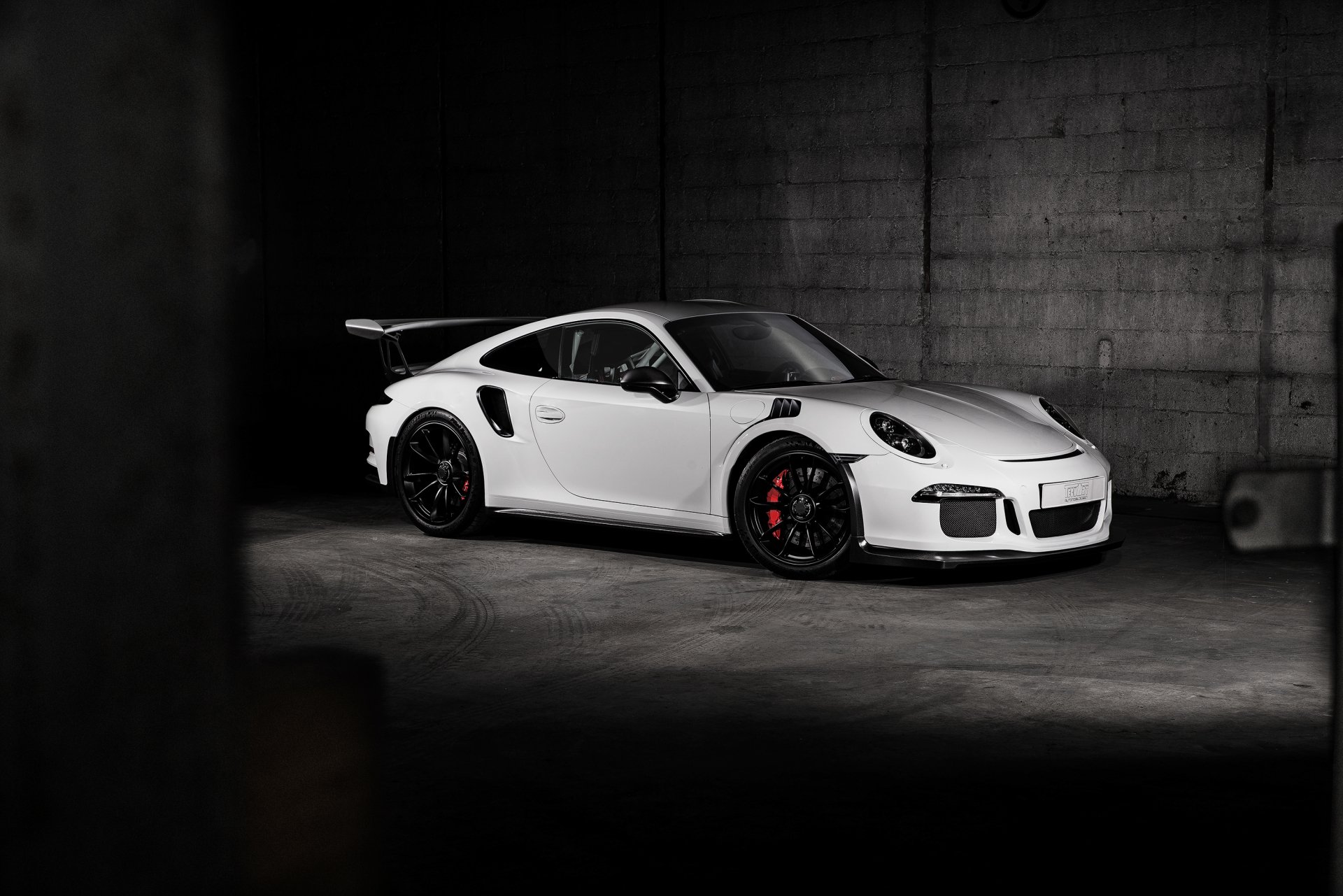 A white Porsche 911 GT3 sports car is showcased in a dimly lit concrete garage, serving as a high-definition PC desktop wallpaper.