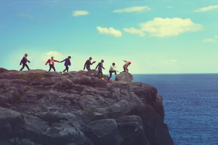 HD desktop wallpaper of the K-pop band BTS walking on a rocky cliff by the sea under a sunny sky. Tags: band, K-pop, Korean, music, BTS.