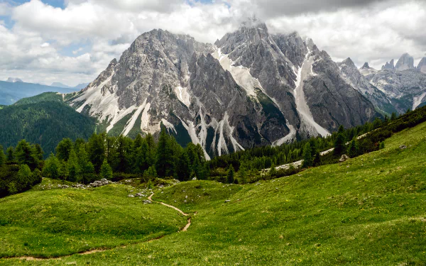 HD PC desktop wallpaper showcasing a vibrant mountain landscape with lush green meadows, rugged peaks, and a partly cloudy sky.