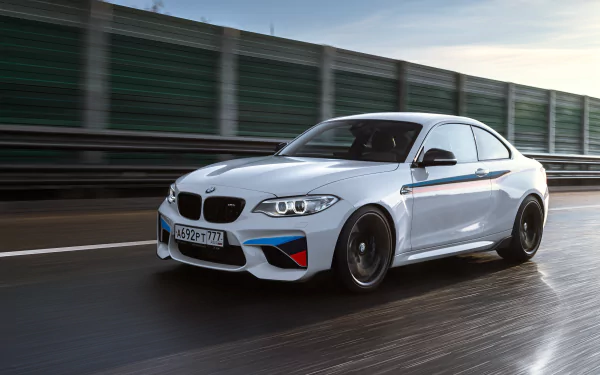 White BMW M2 sports car driving on a wet road, captured in sharp 4K Ultra HD quality, showcasing the vehicle's sleek design and dynamic motion.