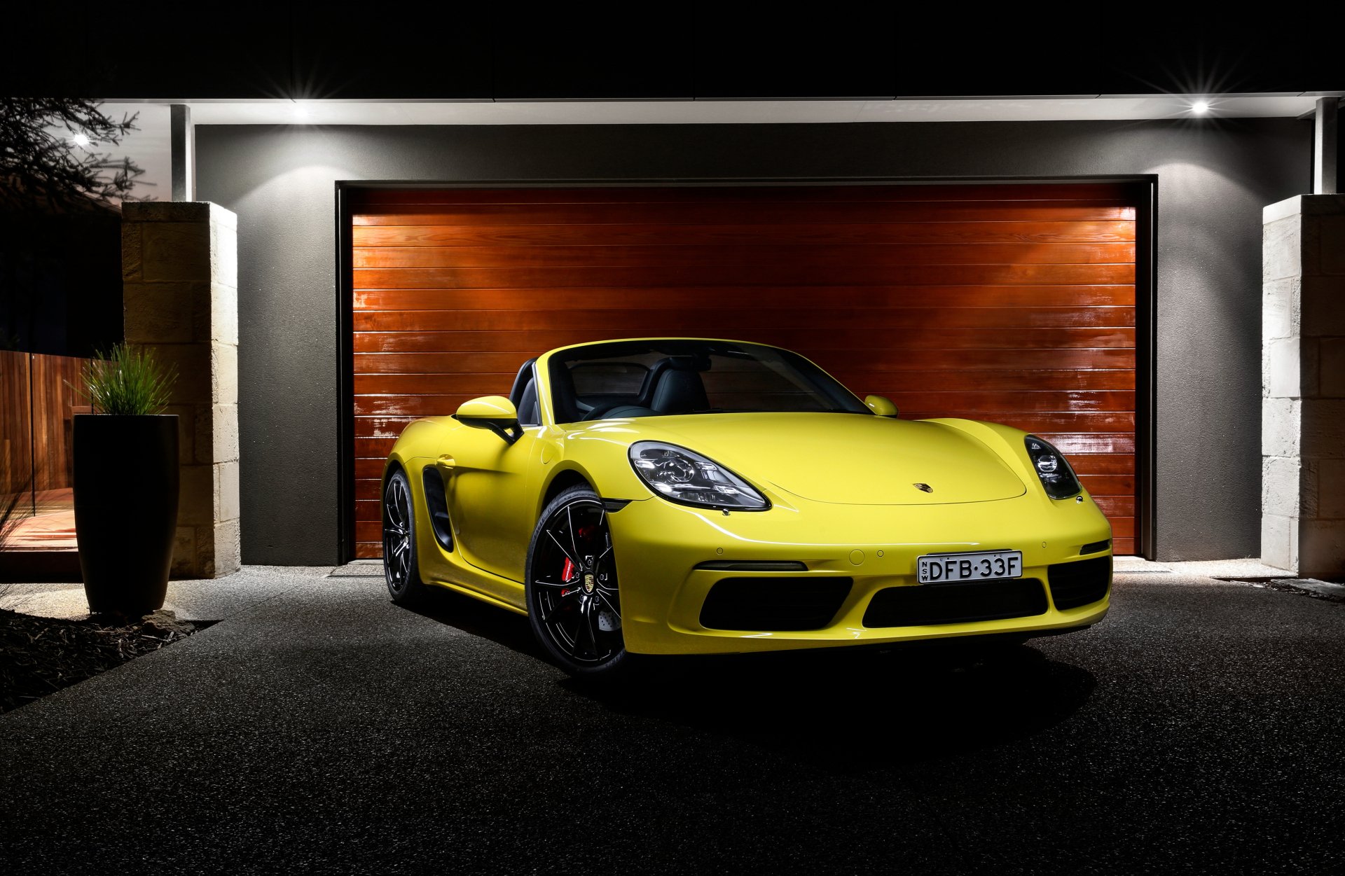 Yellow Porsche Boxster sports car parked in front of a modern garage, showcased in sharp 4K Ultra HD detail for PC desktop wallpaper and background.