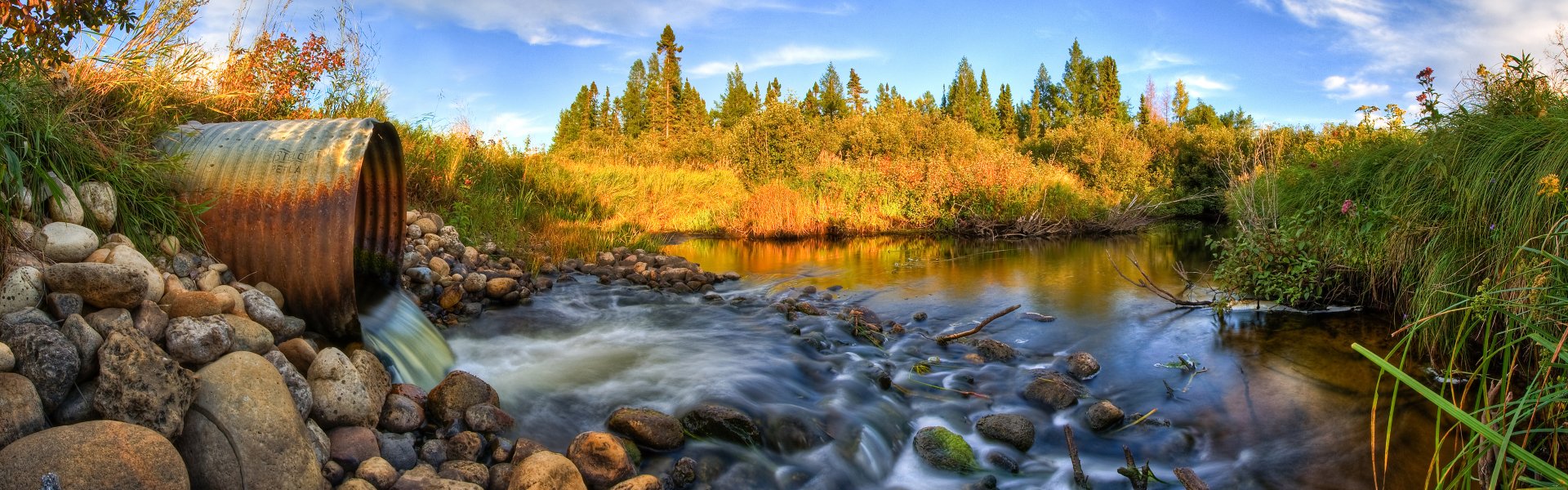 HD desktop wallpaper of a serene nature scene with a flowing stream surrounded by autumnal trees and clear blue sky.