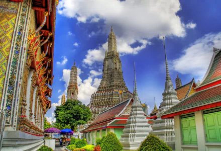 HD desktop wallpaper showcasing the vibrant architecture of Wat Arun temple in Bangkok, Thailand, with intricate details under a bright blue sky on a bustling street.