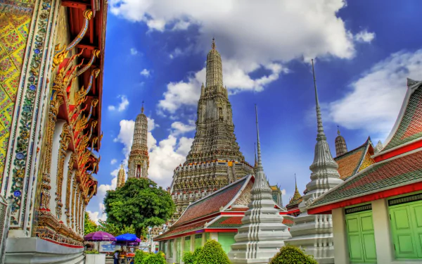 HD desktop wallpaper showcasing the vibrant architecture of Wat Arun temple in Bangkok, Thailand, with intricate details under a bright blue sky on a bustling street.