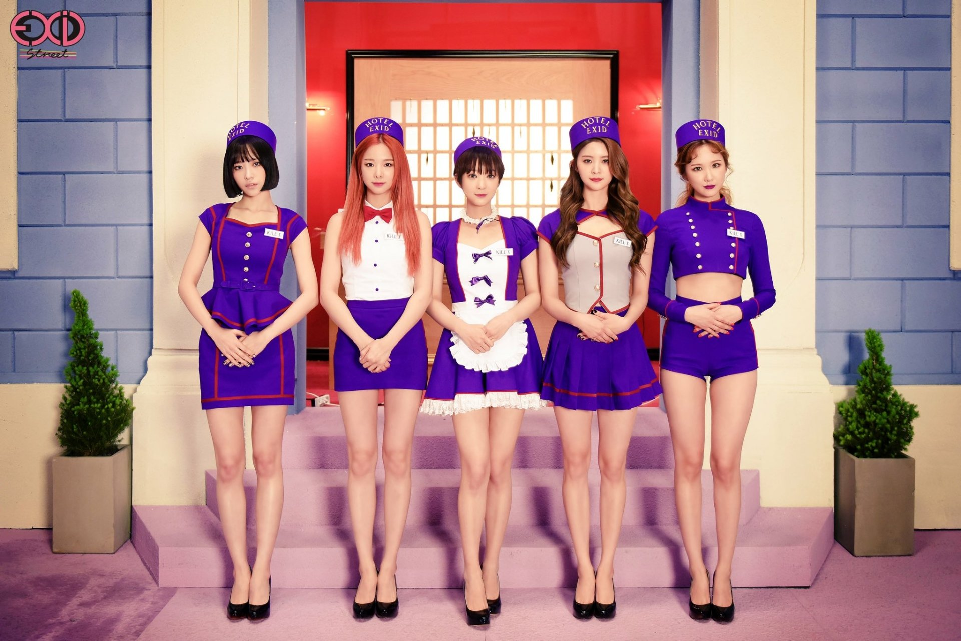 Five members of EXID stand in stylish purple outfits against a colorful backdrop. This HD desktop wallpaper captures their vibrant energy and unique fashion.