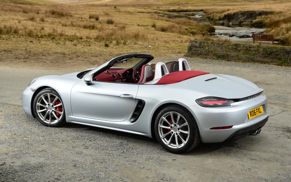 Silver Porsche Boxster convertible with red interior parked on a gravel country lane, HD desktop wallpaper of the sports car.