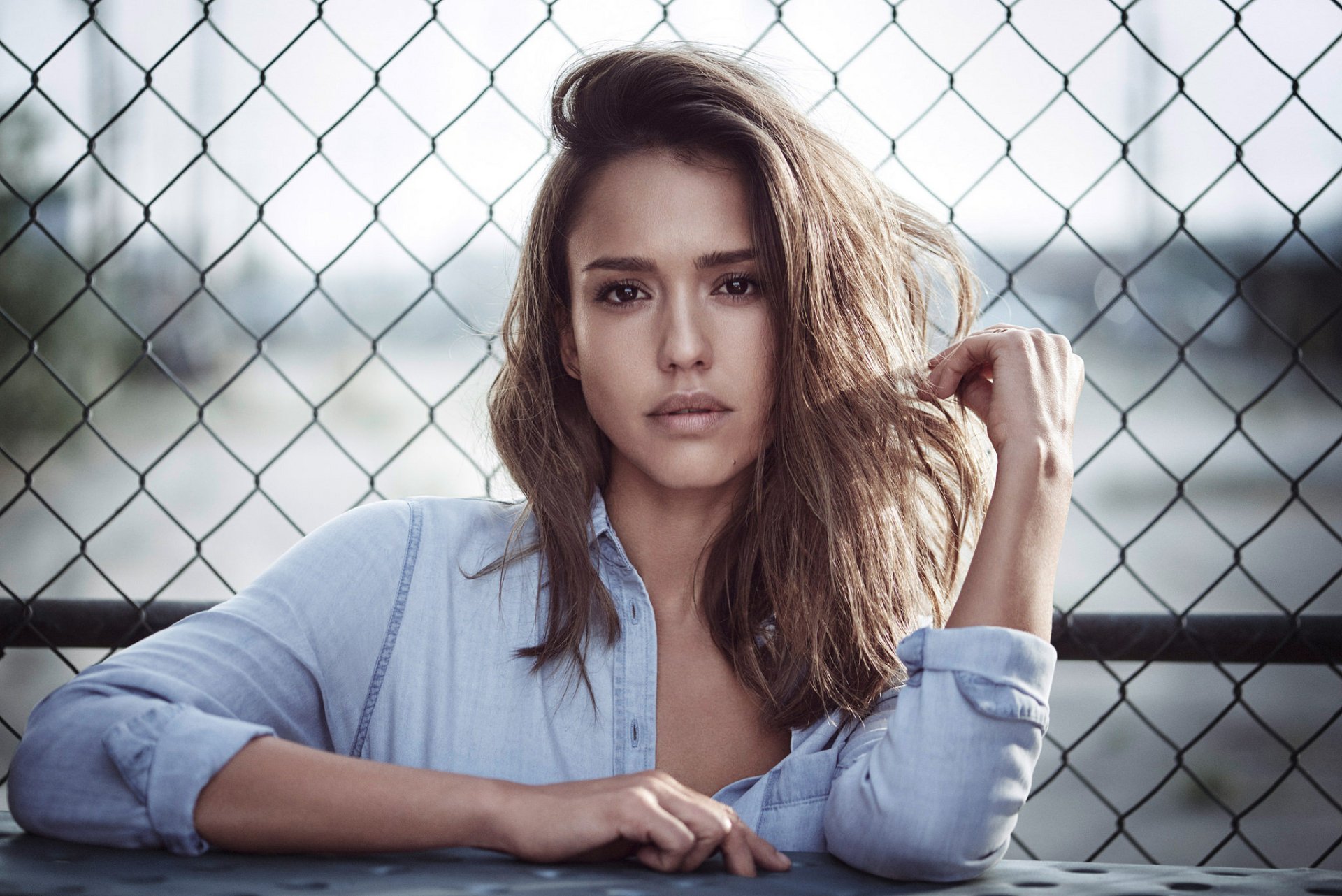 HD desktop wallpaper featuring American actress Jessica Alba with brunette hair and brown eyes, posing confidently in front of a chain-link fence.