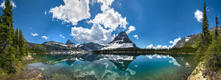 A stunning panoramic view of Glacier National Park in Montana, featuring a tranquil lake that reflects majestic mountains and a vibrant blue sky dotted with clouds.