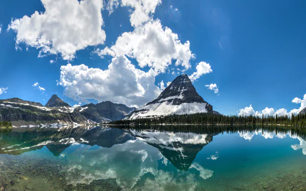 A stunning panoramic view of Glacier National Park in Montana, featuring a tranquil lake that reflects majestic mountains and a vibrant blue sky dotted with clouds.