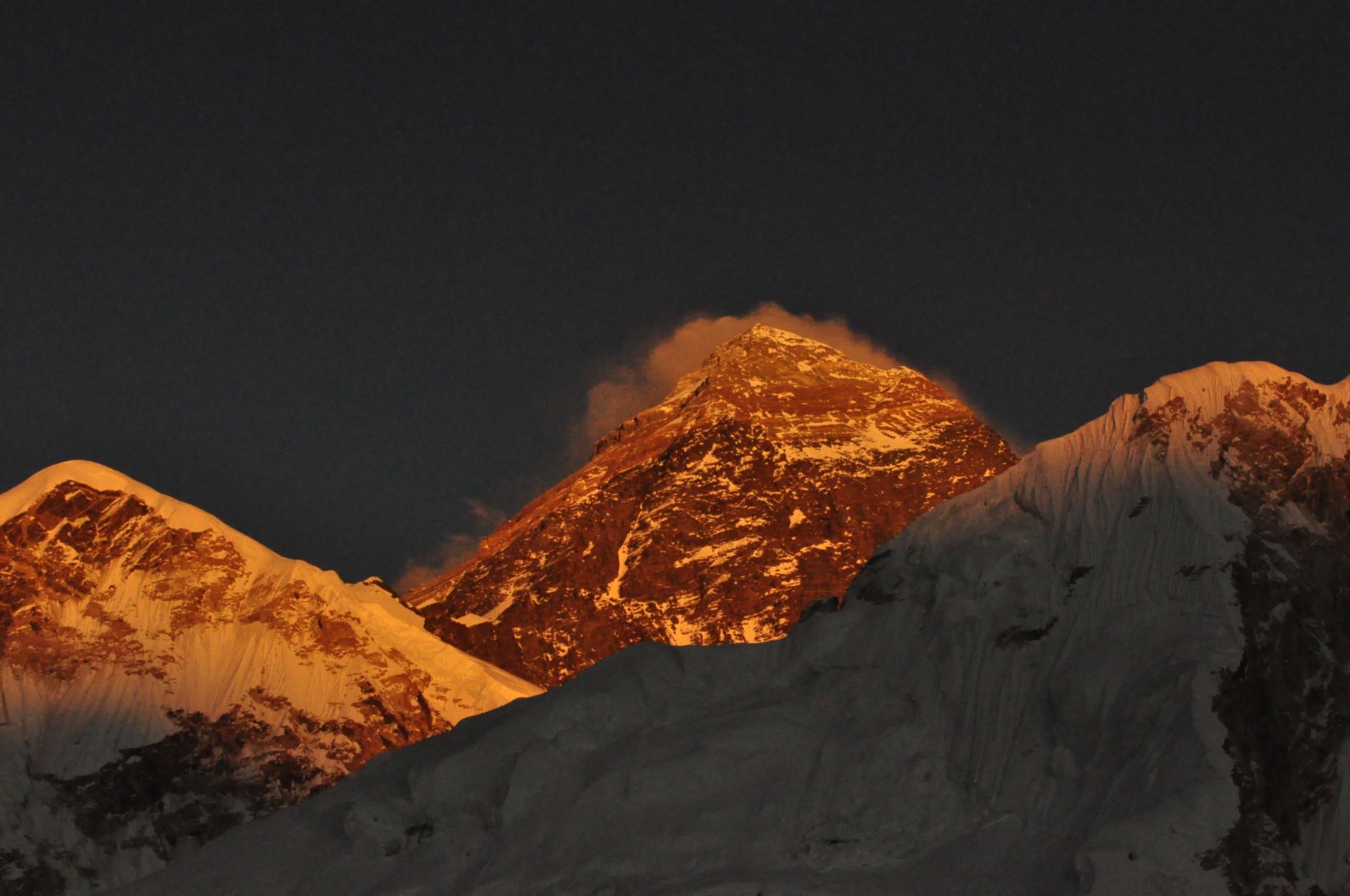 HD desktop wallpaper showcasing Mount Everest at sunset, with snow-covered peaks glowing in warm orange hues against a dark sky.