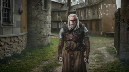 HD desktop wallpaper of a man cosplaying Geralt of Rivia from The Witcher, standing in a medieval village setting with detailed armor and sword.