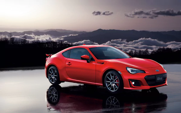 A red Subaru BRZ sports car showcased in a stunning 4K Ultra HD PC desktop wallpaper with a reflective wet surface and dramatic mountainous sky background.