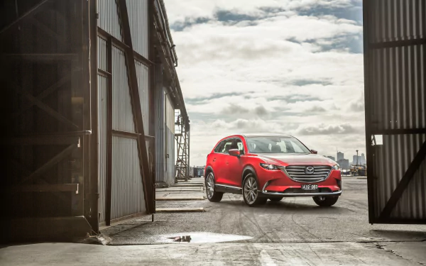 A red Mazda CX-9 SUV is parked in an industrial setting under a cloudy sky, captured in 4K Ultra HD for a PC desktop wallpaper background.