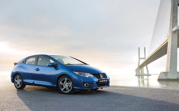 A sleek blue Honda Civic parked beside a modern bridge, set against a serene sky. This HD image captures the compact car's stylish design and urban landscape backdrop.