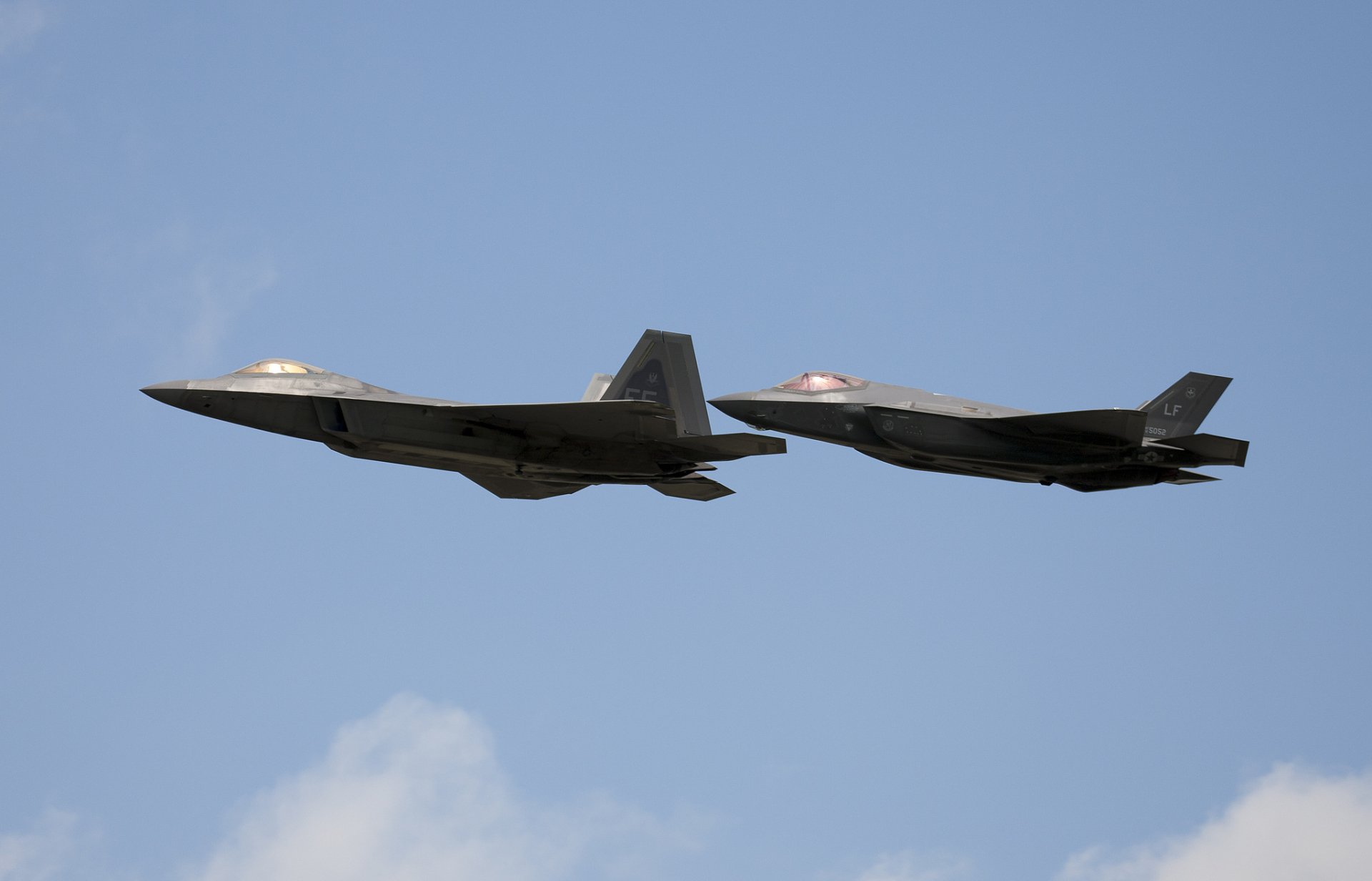 Two advanced military jet fighters, the Lockheed Martin F-22 Raptor and F-35 Lightning II, soar through a clear blue sky, showcasing their sleek designs and capabilities.