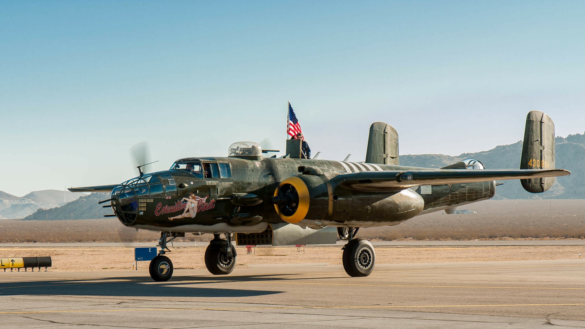HD desktop wallpaper featuring a North American B-25 Mitchell warplane, a military bomber aircraft of the air force, parked on a desert runway under clear skies.