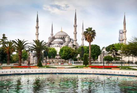 A stunning HD image of the Sultan Ahmed Mosque, showcasing its iconic minarets surrounded by lush greenery and a reflective pool, capturing its religious significance and architectural beauty.