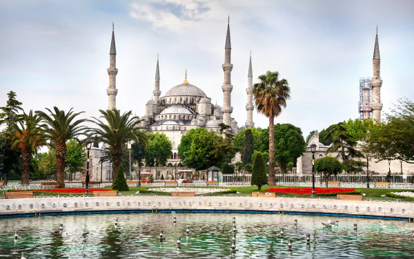 A stunning HD image of the Sultan Ahmed Mosque, showcasing its iconic minarets surrounded by lush greenery and a reflective pool, capturing its religious significance and architectural beauty.