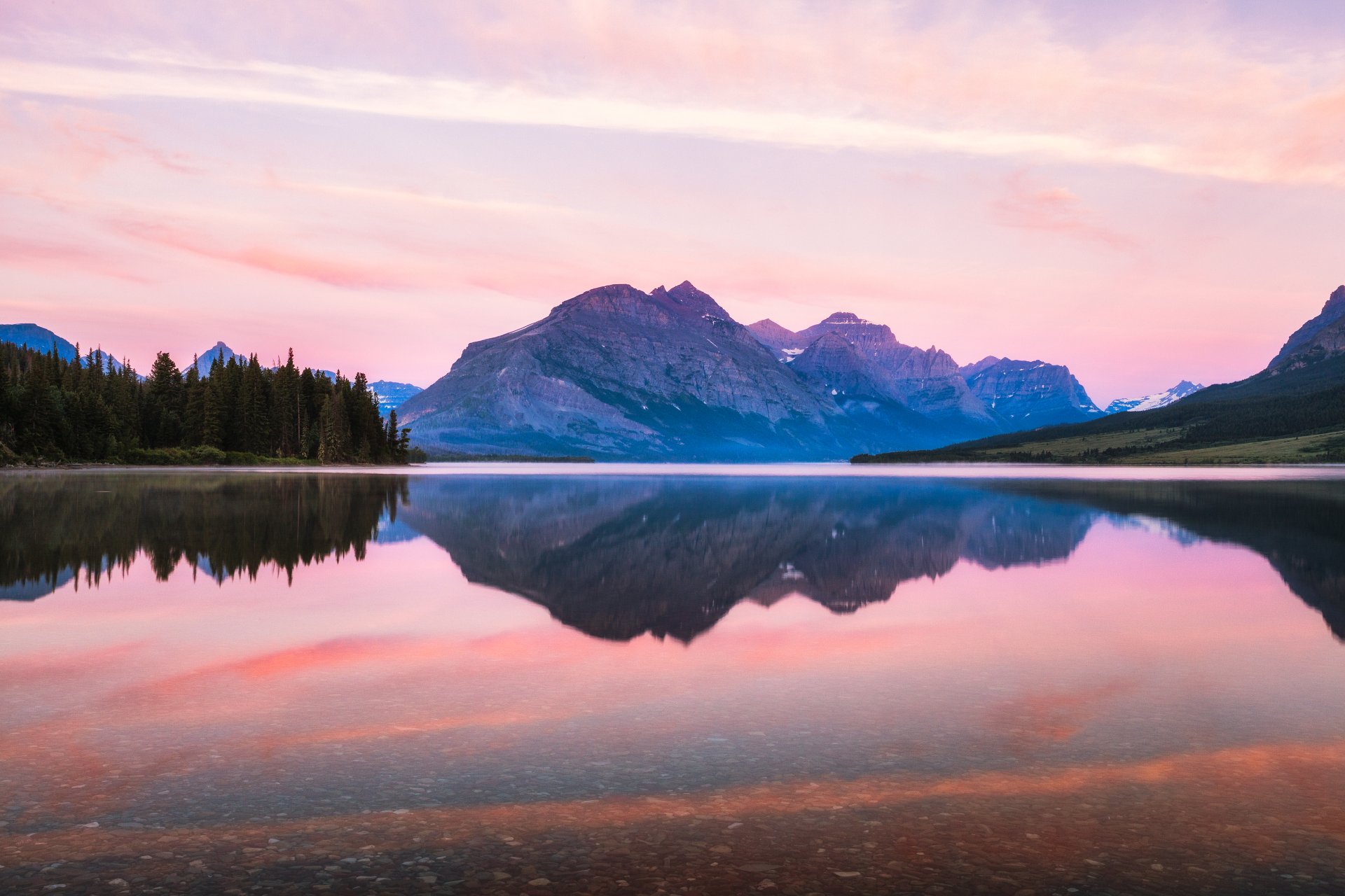 4K Ultra HD PC desktop wallpaper: Glacier National Park mountains at sunset reflected in a calm lake, pink skies and evergreen shoreline forming a sharp mirror image.