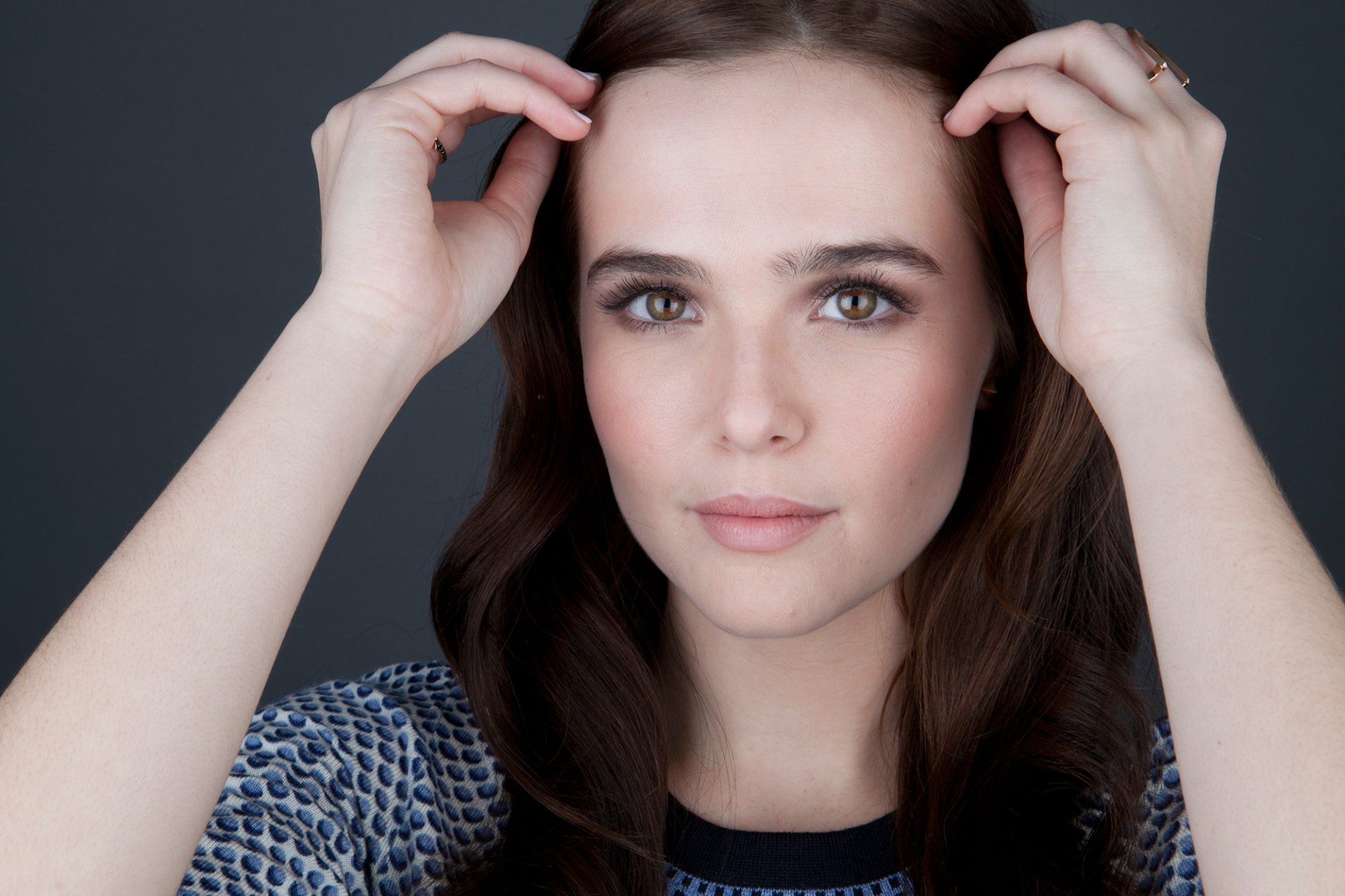 HD desktop wallpaper featuring a close-up portrait of American actress Zoey Deutch with brunette hair and brown eyes against a dark background.