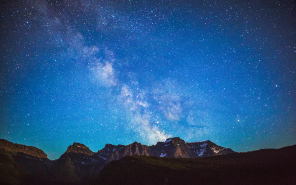 A breathtaking view of the Milky Way stretching across a starry sky above the mountains in Glacier National Park, Montana. This stunning scene captures the beauty of nature at night.