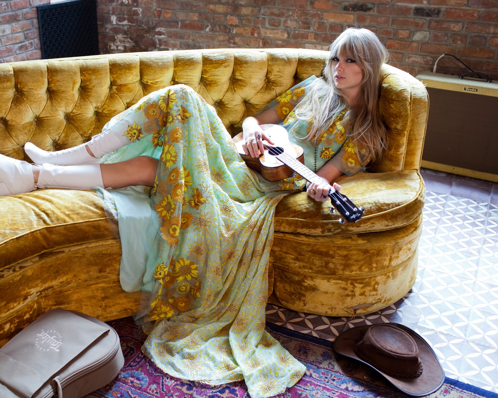A blonde American singer lounges on a vintage yellow couch, wearing a flowing dress and holding a guitar, with blue eyes reflecting her connection to music.