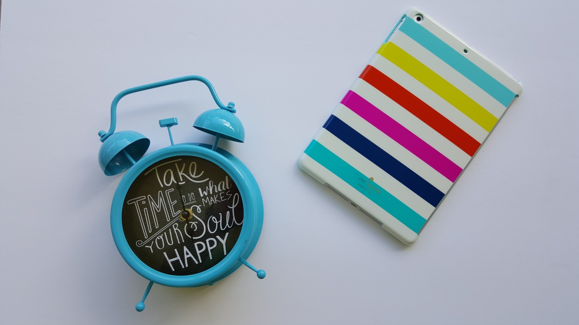 A vibrant blue alarm clock with an inspirational quote next to a colorful striped tablet, creating a motivational desktop wallpaper in 4K Ultra HD.